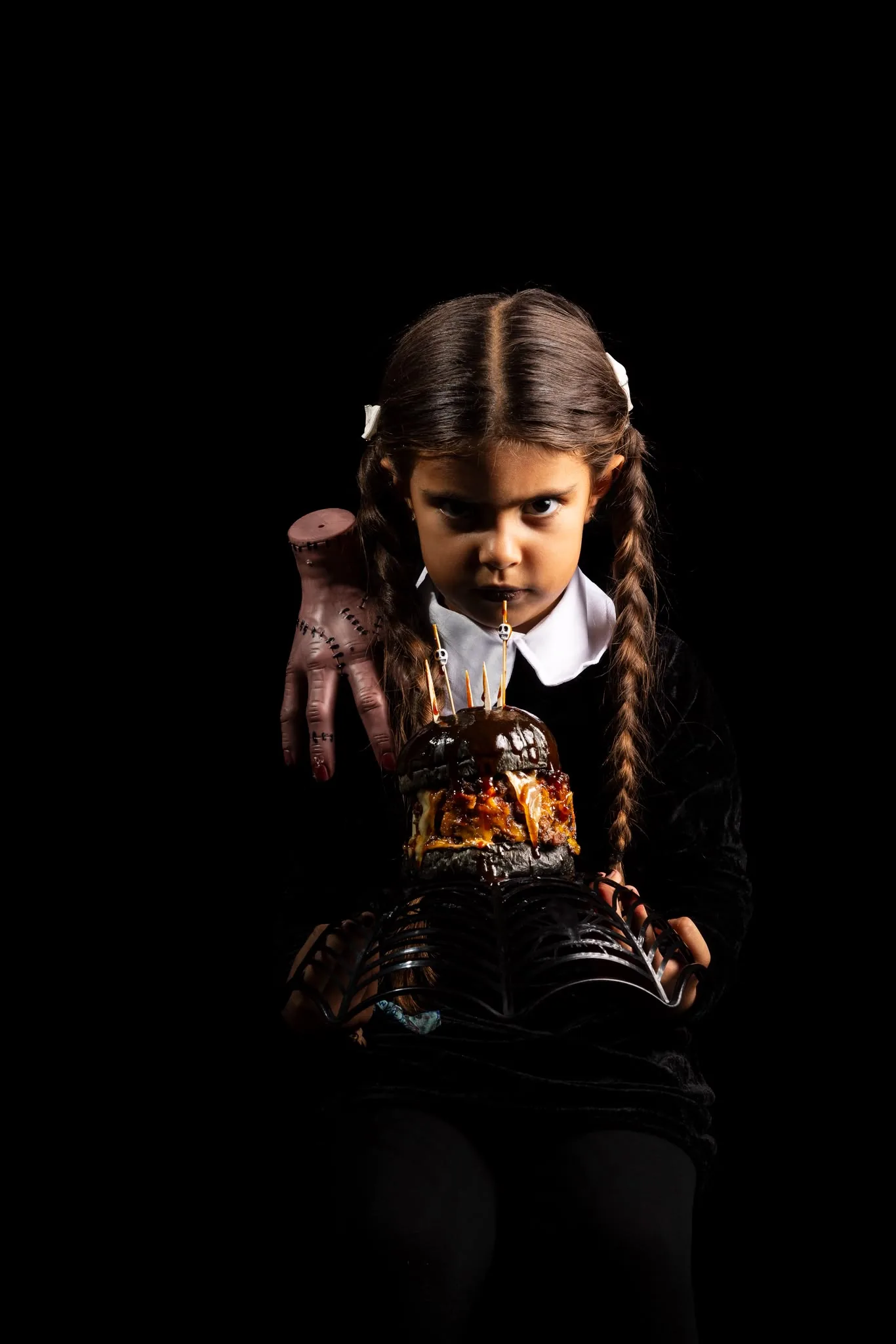 Una niña vestida de negro con coletas sostiene la VUDÚ sobre una bandeja de telaraña, junto a una mano de atrezo